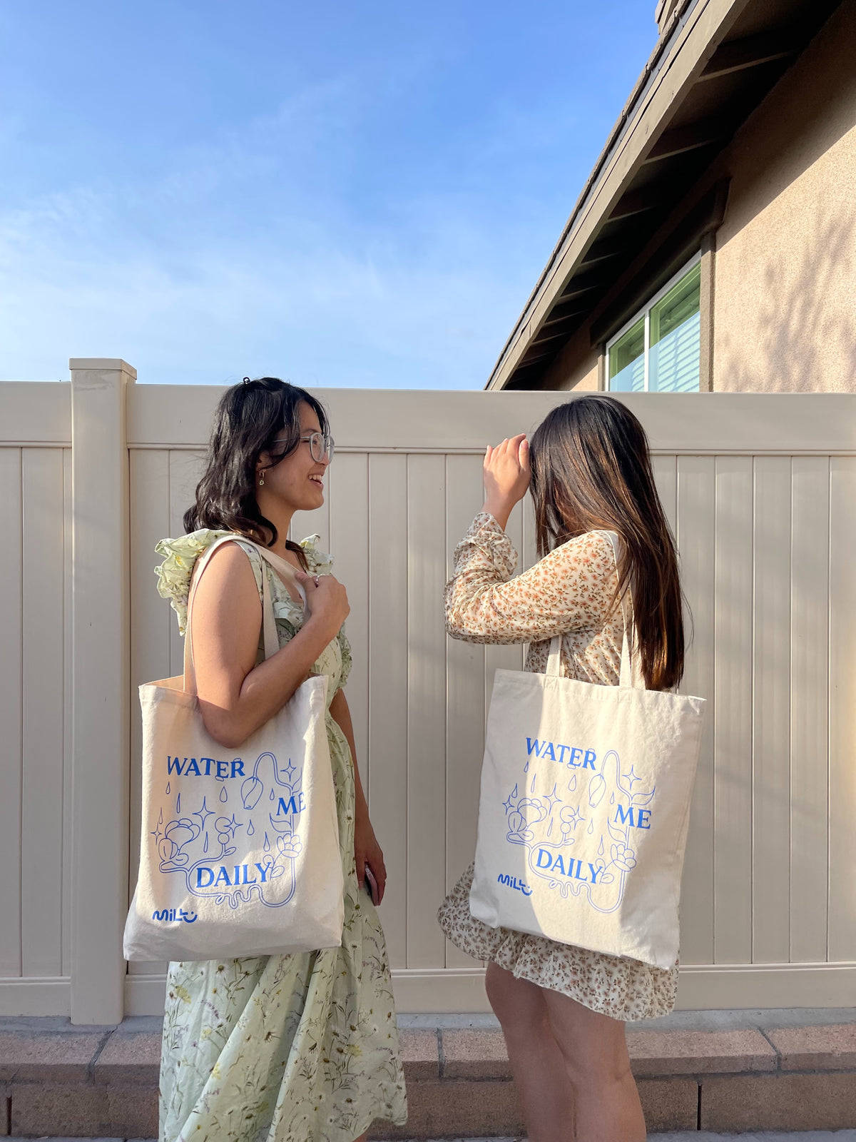 Two people carrying beige MILLU Water Me Daily tote bags over their shoulders outdoors.