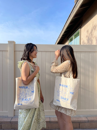 Two people carrying beige MILLU Water Me Daily tote bags over their shoulders outdoors.